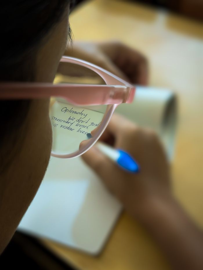 A person writing with handwriting reflected in their glasses, creating an artistic effect.