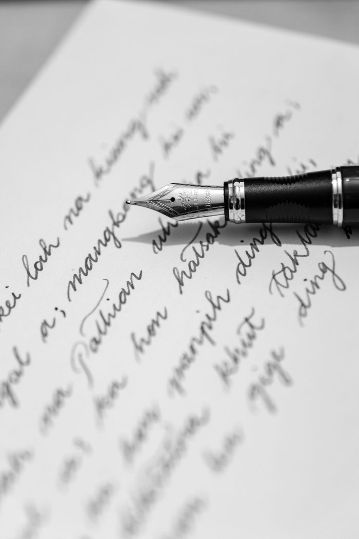 Black and white photo of a fountain pen on a handwritten letter, capturing classic writing elegance.