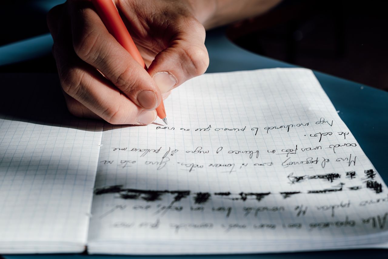 Close-up of a hand writing on a notepad, bathed in sunlight, indoors.
