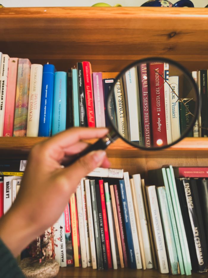 Hand holding magnifying glass focuses on books on a bookshelf, enhancing the details.