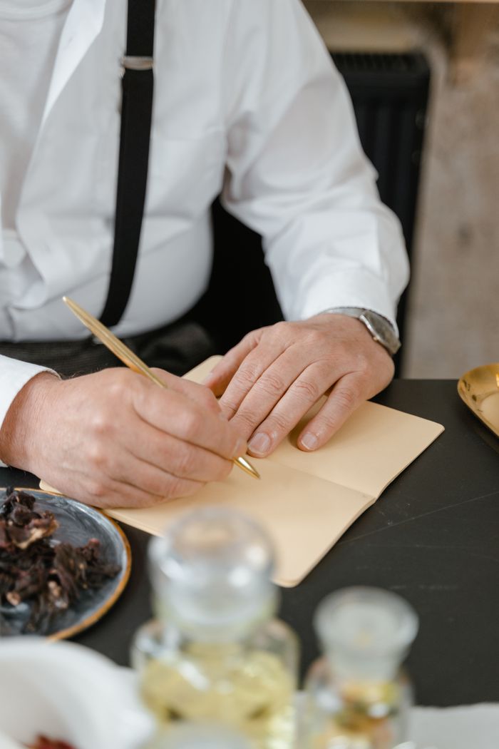 Close-up of a man writing in a notebook at a dining table set with food and drink.